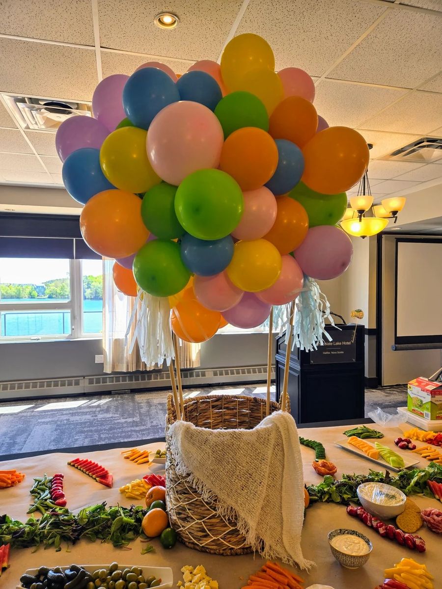 Colourful balloon bunch with a wicker basket over a grazing table