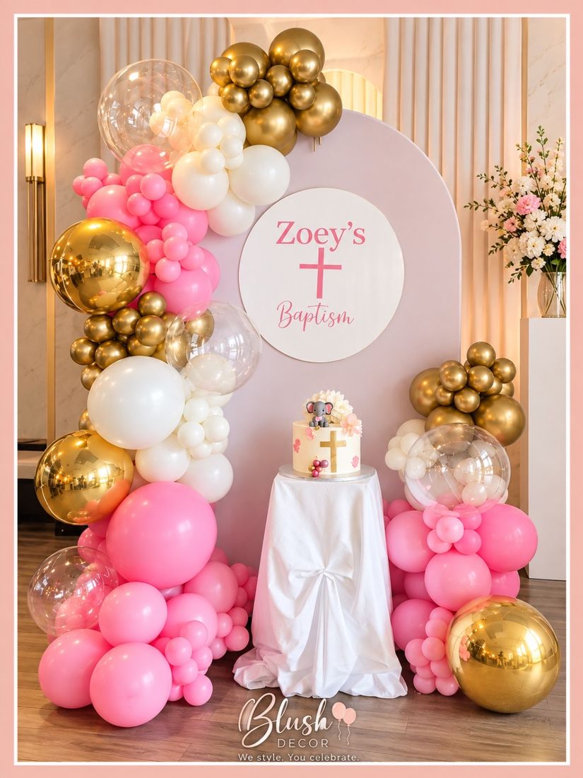 Pink, white and gold baptism backdrop with clear and gold orbs beside a cake table