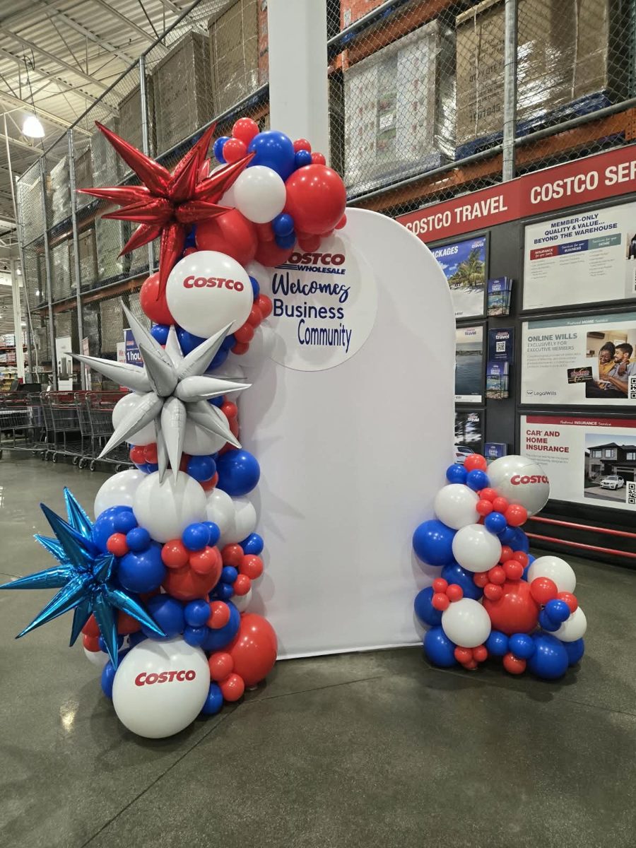 Red, white and blue organic half arch with Costco logo balloons and starbursts around a welcome backdrop