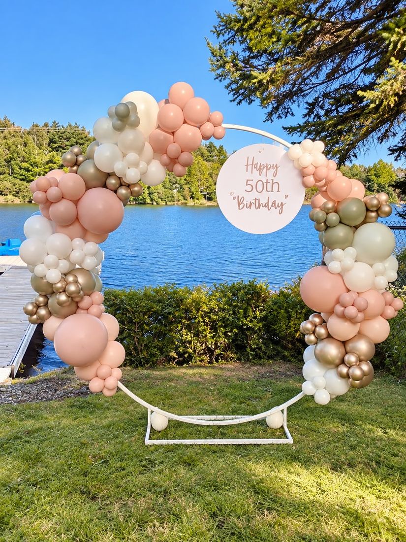 Peach, sage and gold hoop backdrop with a Happy 50th Birthday sign by a lake