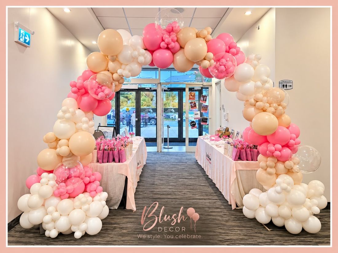 Pink, peach and white organic arch with clear confetti balloons over a vendor market
